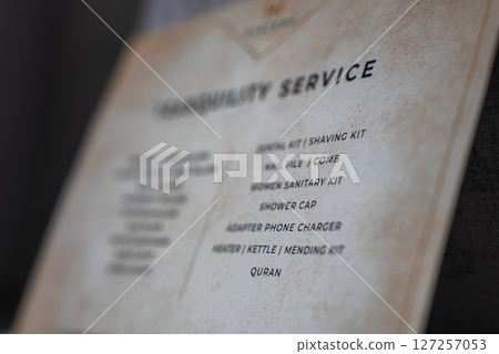 Printed card titled Tranquility Service lists amenities like dental kit, shaving kit, and Quran, set on a beige textured background with a logo. 127257053