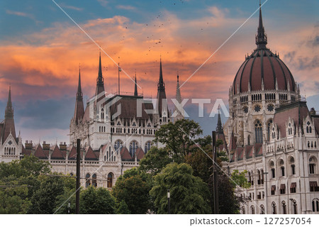 The Hungarian Parliament Building in Budapest, Hungary, features neo Gothic architecture, spires, and a dome, set against a vibrant sunset sky. 127257054