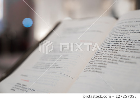 An open book with French text in sharp focus, set indoors. The background features a blurred bokeh effect with a prominent blue light. 127257055