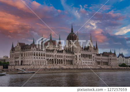 The neo Gothic Hungarian Parliament Building in Budapest stands by the Danube River, with spires and domes reflected in calm waters under a vibrant sky. The neo Gothic Hungarian Parliament Building in Budapest stands by the Danube River, with spires and domes reflected in calm waters under a vibrant sky. 127257059