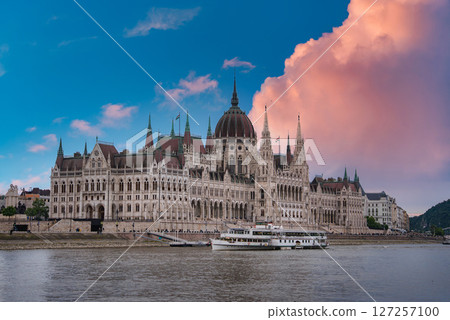 The Hungarian Parliament Building in Budapest stands along the Danube River, with neo Gothic architecture, vibrant clouds, and a docked white boat. The Hungarian Parliament Building in Budapest stands along the Danube River, with neo Gothic architecture, vibrant clouds, and a docked white boat. 127257100