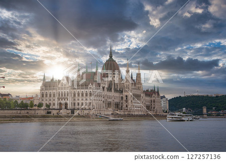 The neo Gothic Hungarian Parliament Building stands by the Danube River in Budapest, with a boat on the water and hills in the background. The neo Gothic Hungarian Parliament Building stands by the Danube River in Budapest, with a boat on the water and hills in the background. 127257136