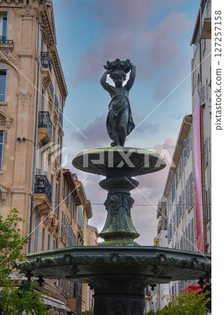 A decorative fountain with a bronze statue of a woman holding a wreath, surrounded by ornate European style buildings in Cannes, France. A decorative fountain with a bronze statue of a woman holding a wreath, surrounded by ornate European style buildings in Cannes, France. 127257158