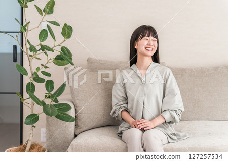 Smiling young Asian woman relaxing in the living room at home 127257534