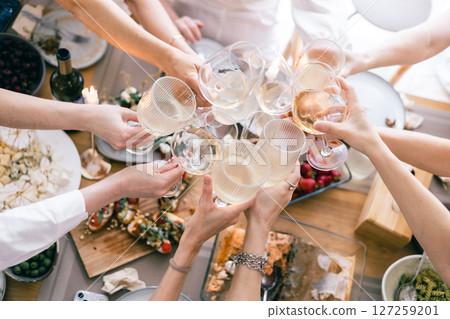 Top view of hands toasting with white wine over festive lunch table with cheese, bruschetta, pasta Top view of hands toasting with white wine over festive lunch table with cheese, bruschetta, pasta 127259201