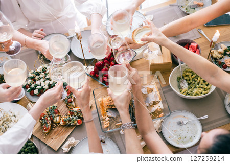 Top view of group cheering with wine over festive table with pasta, bruschetta, cheese, strawberries Top view of group cheering with wine over festive table with pasta, bruschetta, cheese, strawberries 127259214