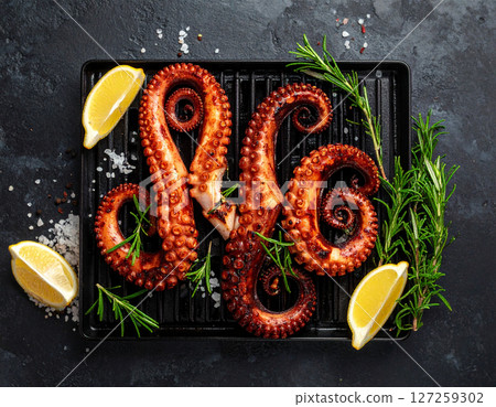 AI generated top view of tender octopus grilled over charcoal, perfectly cooked with smoky aroma and charred edges. Seasoned with salt and black pepper, garnished with fresh rosemary and lemon wedges. 127259302
