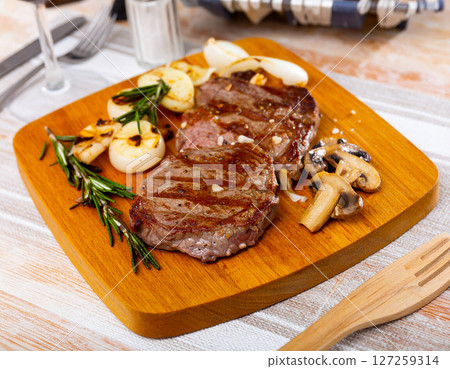 AI generated image of juicy medium rare steak resting on wooden cutting board, served with roasted garlic, onions, rosemary and mushrooms. Drizzled with rich mushroom gravy with salt and black pepper. AI generated image of juicy medium rare steak resting on wooden cutting board, served with roasted garlic, onions, rosemary and mushrooms. Drizzled with rich mushroom gravy with salt and black pepper. 127259314