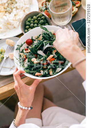 Top view of woman holding fresh green salad with arugula, shrimp and tomatoes at summer lunch table Top view of woman holding fresh green salad with arugula, shrimp and tomatoes at summer lunch table 127259328