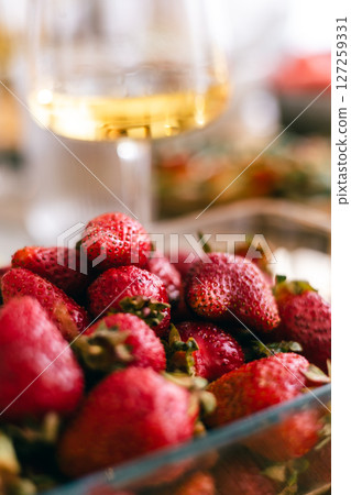 Fresh ripe strawberries in glass bowl with wine glass in soft focus background, summer fruit concept 127259331