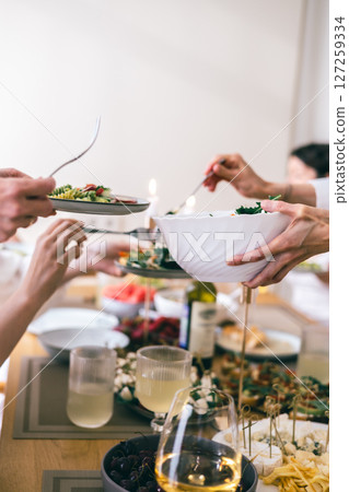 Hands serving pasta and salad at festive lunch table with wine, cheese, and snacks in cozy gathering 127259334