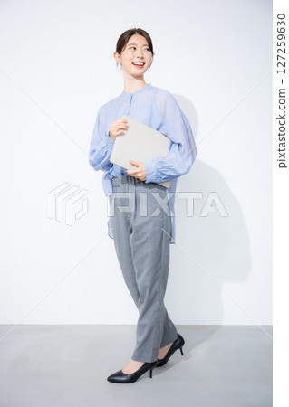 一位身穿淺藍色透明襯衫的女士，白色背景上手持筆記型電腦，回頭望去。圖片為工作調動、人事等招募。 127259630