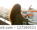 back view, curly girl stands in apartment on balloon with city view, holds phone in hands at sunset, communication, correspondence, online shopping, remote work, freelancer 127260521
