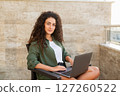 Portrait of a beautiful curly woman working on a laptop, looking at the camera, working on the Internet, online shopping, social networking, online learning, freelancer 127260522