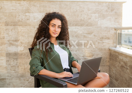 Portrait of a beautiful curly woman working on a laptop, looking at the camera, working on the Internet, online shopping, social networking, online learning, freelancer 127260522