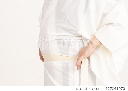 A man dressing himself in a kimono, tying the waist cord of his undergarment A man dressing himself in a kimono, tying the waist cord of his undergarment 127261070
