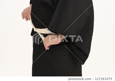 A man dressing himself in a kimono, tying the waist cord 127261075