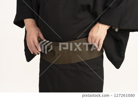 A man dressing himself in a kimono, adjusting his obi 127261080