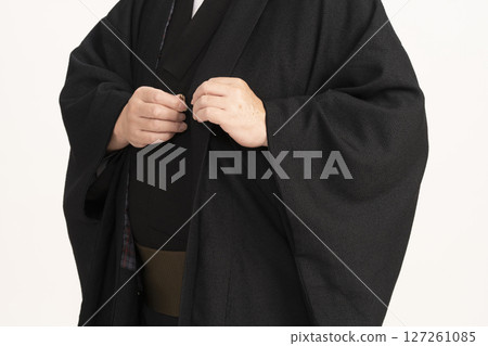 A man dressing himself in a kimono, hands tying a haori cord 127261085