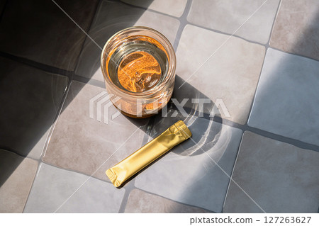 Glass of Water and Golden Sachet on a Tiled Surface. Energy Diet and Healthy Lifestyle Concepts. 127263627