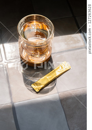 Gold Energy Drink Powder Packet on Tile Surface Next to a Glass of Water. Concept for Diet and Health. 127263628