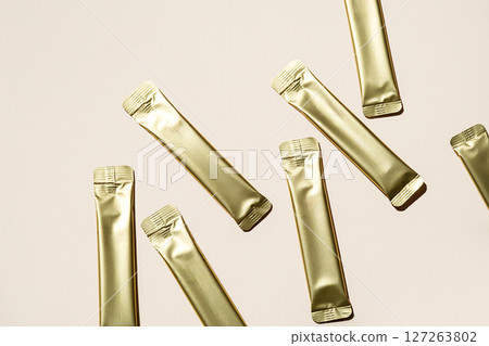 Several Golden Stick Packaging Sachets on Light Background. Unbranded Foil Pouch Mockup for Product Presentation. 127263802