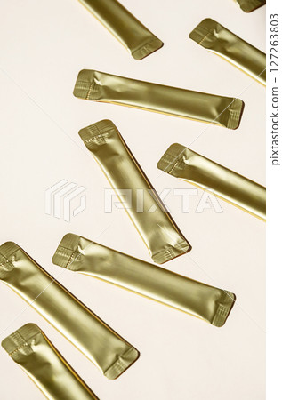 Golden Metallic Stick Packaging on Light Background. Small Packets for Food, Medicine or Cosmetic Product. Golden Metallic Stick Packaging on Light Background. Small Packets for Food, Medicine or Cosmetic Product. 127263803