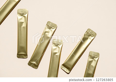 Multiple Golden Foil Stick Packs and Sachets on Beige Background. Mockup for a Quick Food Product, Skincare or Medicine. 127263805