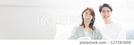 A young couple relaxing in a brightly lit living room, looking at the camera, banner for the image of a married couple or newlyweds A young couple relaxing in a brightly lit living room, looking at the camera, banner for the image of a married couple or newlyweds 127263808