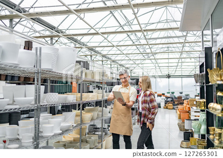 A store employee assists a female customer in a garden shop with a wide selection of flowerpots. A store employee assists a female customer in a garden shop with a wide selection of flowerpots. 127265301