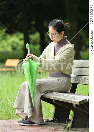 一位微笑的日本女性坐在長椅上，撐著傘 127265875
