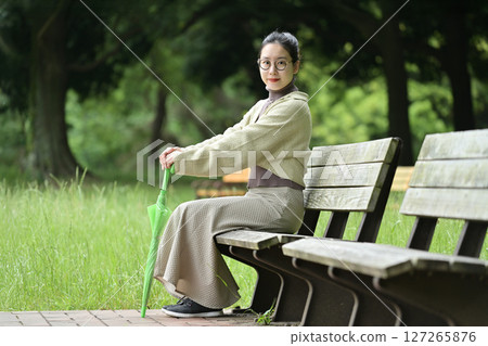A smiling Japanese woman sitting on a bench and holding an umbrella 127265876