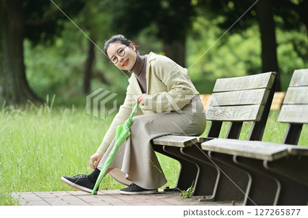 A smiling Japanese woman sitting on a bench and holding an umbrella 127265877