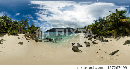 A hidden beach featuring soft sand, scattered rocks, clear water, and surrounded by dense tropical vegetation under a cloudy sky. Butzel Beach. Mahe, Seychelles. VR 360. 127267499