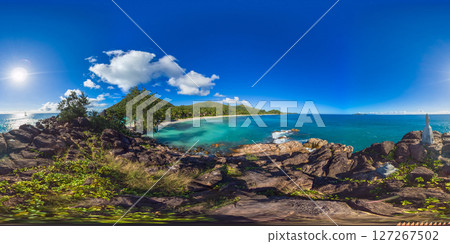 A vibrant coastal scene with rocks, clear waters and green hills extending along the shoreline under a bright sky. Praslin, Seychelles. Constance Lemuria Beach. 360 Degree view. A vibrant coastal scene with rocks, clear waters and green hills extending along the shoreline under a bright sky. Praslin, Seychelles. Constance Lemuria Beach. 360 Degree view. 127267502