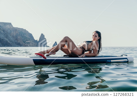 Woman Paddleboard Ocean - A young woman relaxes on a paddleboard in a calm ocean, enjoying the tranquil scenery. Woman Paddleboard Ocean - A young woman relaxes on a paddleboard in a calm ocean, enjoying the tranquil scenery. 127268321