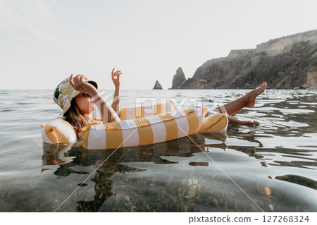 Woman Float Sea Relaxing on inflatable ring in sea against rocky cliff. 127268324