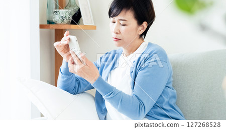 Middle-aged woman looking at a smartphone in the living room Middle-aged woman looking at a smartphone in the living room 127268528