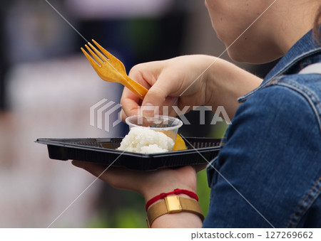 Close-Up of Person Eating Meal from Plastic Container with Utensil Outdoors 127269662