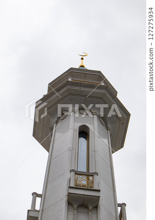 View from below of the beautiful white stone minaret of the mosque with geometric patterns on the walls and a crescent moon rising against the sky 127275934