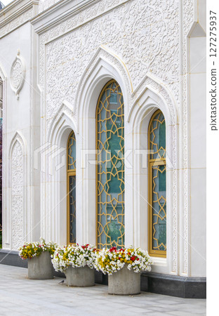 The white stone wall of the mosque with traditional Arabic floral ornamentation and large stained glass windows 127275937