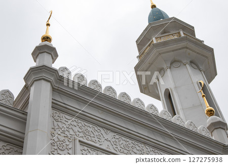 View from below of the beautiful white stone minaret of the mosque with geometric patterns on the walls and a crescent moon rising against the sky 127275938