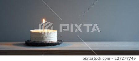 Single lit candle on white frosted cake against gray backdrop, minimalistic birthday celebration concept 127277749
