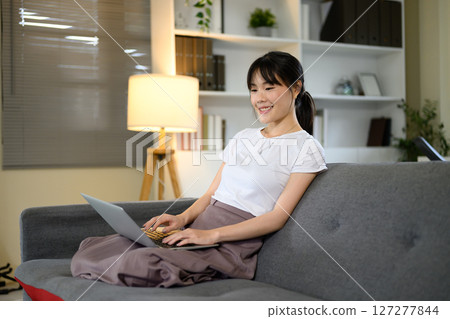 Young woman relaxing with laptop computer in living room Young woman relaxing with laptop computer in living room 127277844
