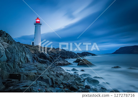 Lighthouse is on a rocky shoreline with a cloudy sky in the background. 127278716