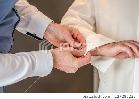 Man groom tying cufflinks on shirt sleeves getting dressed with closeup of hands no face 127280223