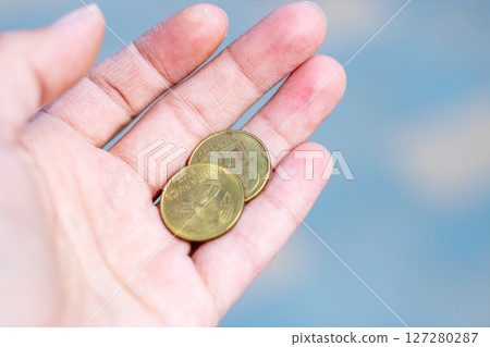 A person is expertly holding two shiny coins in the palm of their hand A person is expertly holding two shiny coins in the palm of their hand 127280287