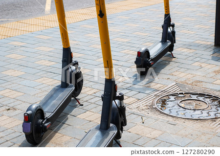 There are two scooters parked on the sidewalk right next to a manhole cover 127280290