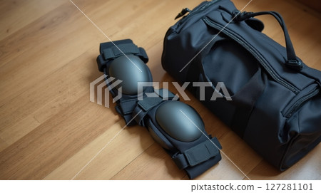 Knee pads next to a sports bag on a wooden floor 127281101