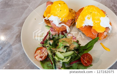 close up of two pieces of egg Benedict with hollandaise sauce and smoked salmon, salad with dressing on the side close up of two pieces of egg Benedict with hollandaise sauce and smoked salmon, salad with dressing on the side 127282075